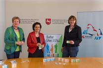Imke Schmieta, Magdalene Linz und Dr. Carola Reimann präsentieren die neuen Care Packs zum Start der Safer Use Kampagne. Auf einem Tisch vor den drei Personen liegen die verfügbaren Packs