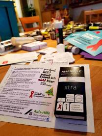 Postkarte mit aufgeklebten Terminen für HIV Schnelltest und aufgeklebtem Kondom in Pappschachtel